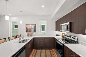 Kitchen featuring appliances with stainless steel finishes, light wood-type flooring, a kitchen breakfast bar, sink, and pendant lighting