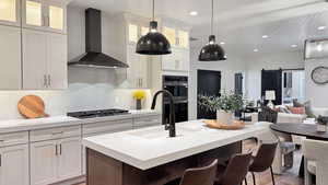 Kitchen with wall chimney exhaust hood, a barn door, appliances with stainless steel finishes, light stone counters, and white cabinetry