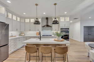 Kitchen with white cabinets, stainless steel appliances, a kitchen island with sink, and wall chimney exhaust hood