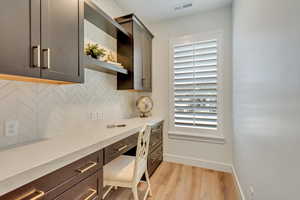 Kitchen with built in desk, backsplash, light hardwood / wood-style flooring, and light stone counters