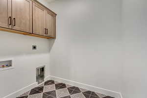 Clothes washing area with electric dryer hookup, hookup for a washing machine, dark tile patterned floors, and cabinets