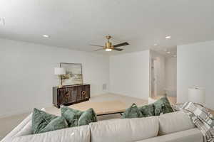 Living room with carpet, a textured ceiling, and ceiling fan