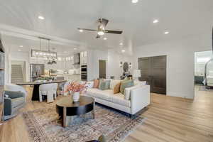 Living room with light hardwood / wood-style flooring and ceiling fan with notable chandelier