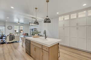 Kitchen featuring light brown cabinetry, a kitchen island with sink, sink, white cabinets, and hanging light fixtures