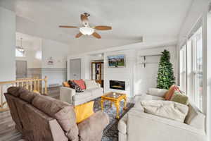 Living room with light wood-type flooring, a large fireplace, vaulted ceiling, ceiling fan, and wood walls