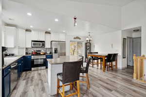 Kitchen with white cabinetry, stainless steel appliances, light hardwood / wood-style flooring, blue cabinets, and a kitchen island