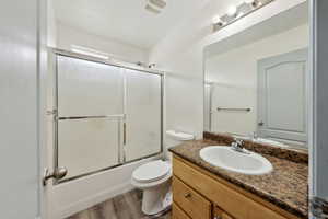 Full bathroom with wood-type flooring, vanity, toilet, and bath / shower combo with glass door