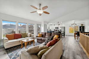 Living room with ceiling fan with notable chandelier, light hardwood / wood-style floors, and vaulted ceiling