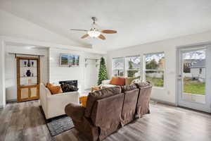 Living room featuring hardwood / wood-style floors, a large fireplace, vaulted ceiling, and ceiling fan