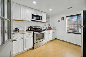 Kitchen with light wood-type flooring, stainless steel appliances, and white cabinetry