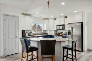 Kitchen featuring a kitchen bar, appliances with stainless steel finishes, a center island, and white cabinetry