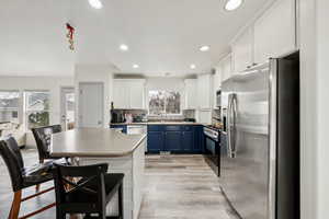 Kitchen featuring white cabinets, light wood-type flooring, blue cabinetry, tasteful backsplash, and stainless steel appliances