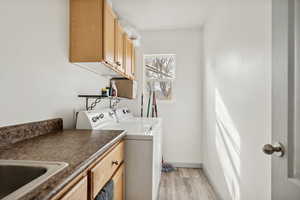 Laundry room featuring washer and dryer, light hardwood / wood-style flooring, cabinets, and sink