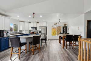 Kitchen with stainless steel appliances, blue cabinets, vaulted ceiling, a kitchen bar, and a kitchen island