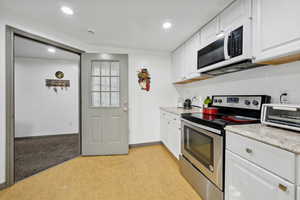 Kitchen with white cabinets, light hardwood / wood-style floors, light stone counters, and appliances with stainless steel finishes