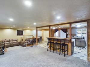 Kitchen with light carpet, a breakfast bar, a textured ceiling, and sink