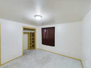 Unfurnished bedroom featuring a walk in closet, light colored carpet, and a closet