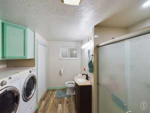 Bathroom with vanity, a textured ceiling, wood-type flooring, separate washer and dryer, and a shower with shower door