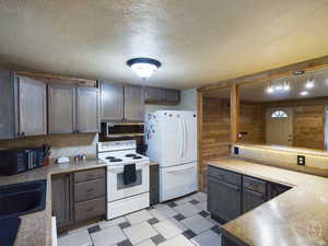 Kitchen with wood walls, a textured ceiling, decorative light fixtures, white appliances, and decorative backsplash