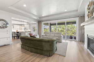 Living room with light wood-type flooring, a tray ceiling, and a healthy amount of sunlight