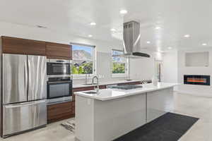 Kitchen featuring sink, stainless steel appliances, tasteful backsplash, island exhaust hood, and an island with sink