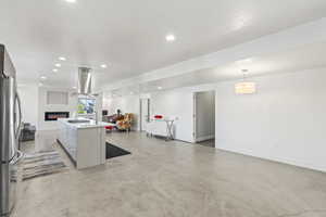 Kitchen with a center island with sink, decorative light fixtures, island exhaust hood, and stainless steel refrigerator