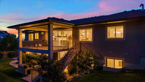 Back house at dusk with a yard and a balcony