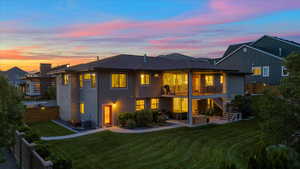 Back house at dusk with a yard, a balcony, and central AC unit