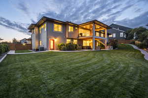 Back house at dusk featuring a balcony, a yard, and central AC