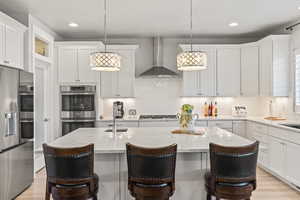 Kitchen with a kitchen island with sink, sink, hanging light fixtures, and wall chimney range hood