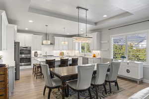 Dining area with a raised ceiling, sink, a notable chandelier, and light wood-type flooring