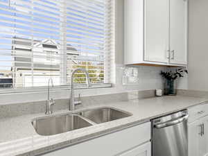 Kitchen with light stone counters, decorative backsplash, sink, white cabinets, and dishwasher