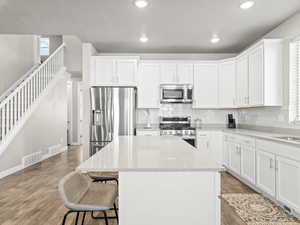 Kitchen with white cabinetry, light stone countertops, stainless steel appliances, and light hardwood / wood-style flooring