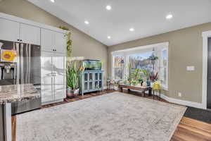 Kitchen featuring lofted ceiling, white cabinetry, light stone countertops, and stainless steel refrigerator with ice dispenser