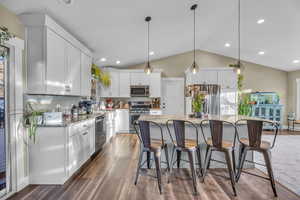 Kitchen featuring a center island, lofted ceiling, white cabinets, dark hardwood / wood-style flooring, and stainless steel appliances