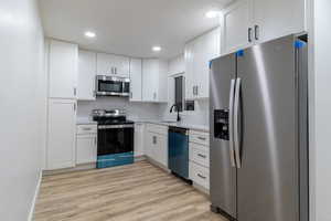 Upstairs Kitchen featuring sink, white cabinets, stainless steel appliances, and light wood-type flooring