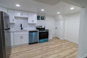 Downstairs Kitchen with white cabinets, light hardwood / wood-style floors, sink, and appliances with stainless steel finishes