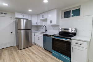 Downstairs Kitchen featuring white cabinetry, sink, stainless steel appliances, decorative backsplash, and light wood-type flooring