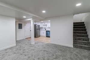 Basement featuring stainless steel fridge, sink, light carpet, and electric panel