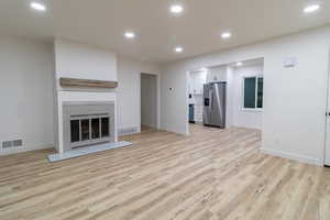 Open concept living room with light wood-type flooring, custom mantle, and wood-burning fireplace!