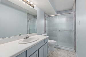 Bathroom with walk in shower, vanity, toilet, and a textured ceiling