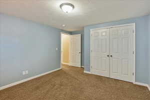 Unfurnished bedroom featuring a textured ceiling, a closet, baseboards, and carpet floors