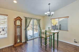 Dining area with plenty of natural light, vaulted ceiling, dark hardwood / wood-style flooring, and an inviting chandelier