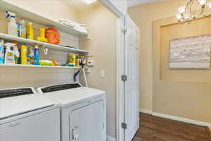 Washroom with a chandelier, washer and dryer, and dark wood-type flooring