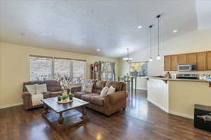 Living room with a chandelier, lofted ceiling, dark wood-type flooring, and a healthy amount of sunlight