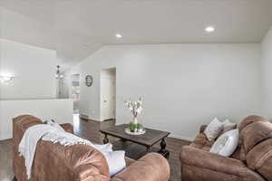 Living room with baseboards, recessed lighting, dark wood-type flooring, visible vents, and lofted ceiling