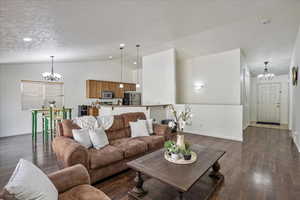 Living area with a chandelier, dark wood-type flooring, baseboards, and vaulted ceiling