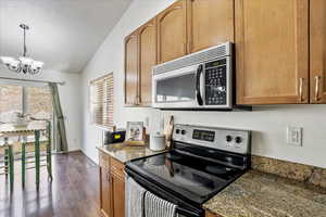 Kitchen with an inviting chandelier, dark wood-style floors, brown cabinets, vaulted ceiling, and stainless steel appliances