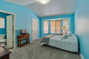 Carpeted bedroom with a textured ceiling, ensuite bath, and lofted ceiling