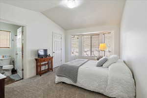 Carpeted bedroom with baseboards, connected bathroom, and vaulted ceiling